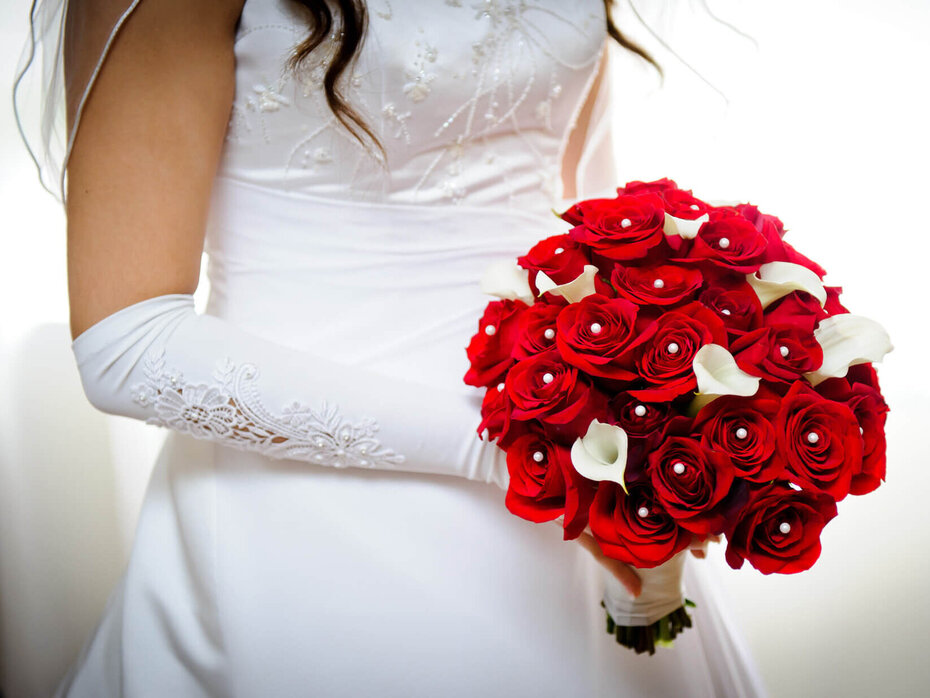 Braut mit eleganten Brauthandschuhen hält roten Brautstrauß