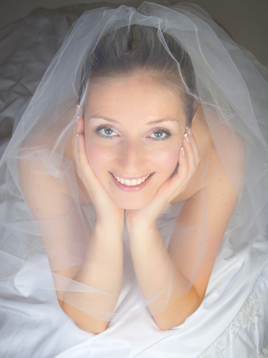 Lächelnde Braut mit Schleier vor dem Gesicht