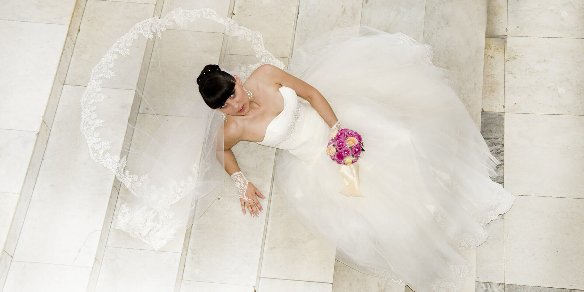 Braut sitzt mit ausgebreitetem Schleier auf der Treppe
