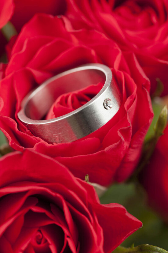 Ein Verlobungsring liegt auf einem Strauß roter Rosen