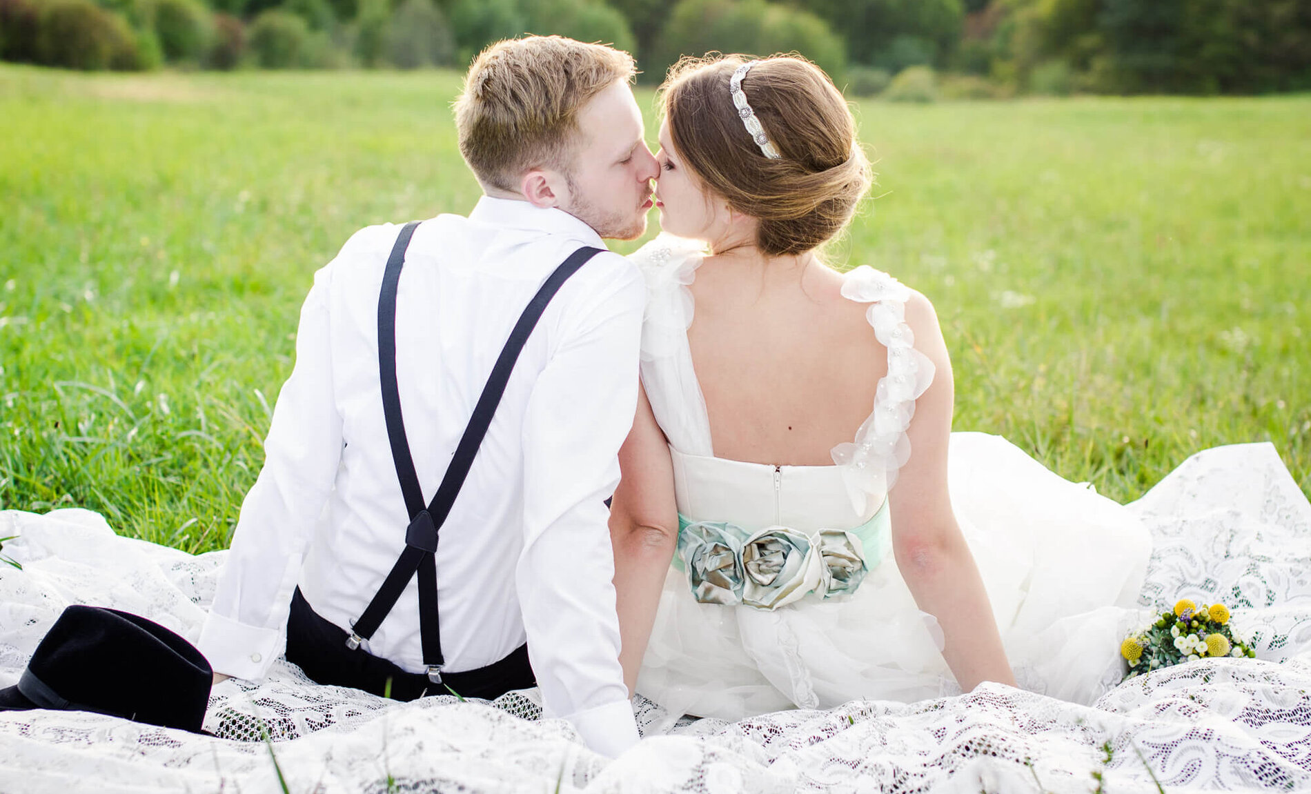 Brautpaar sitzt auf der Wiese und küsst sich
