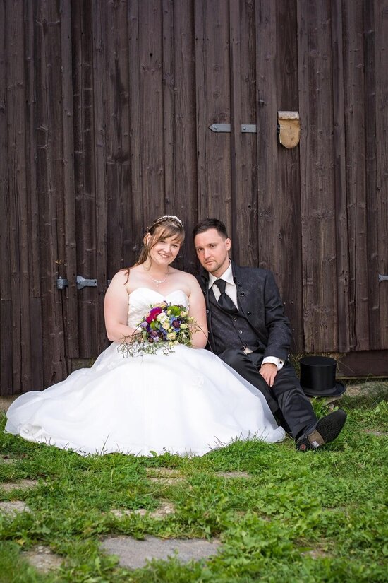 Brautpaar sitzt auf der Wiese vor einer Schneue