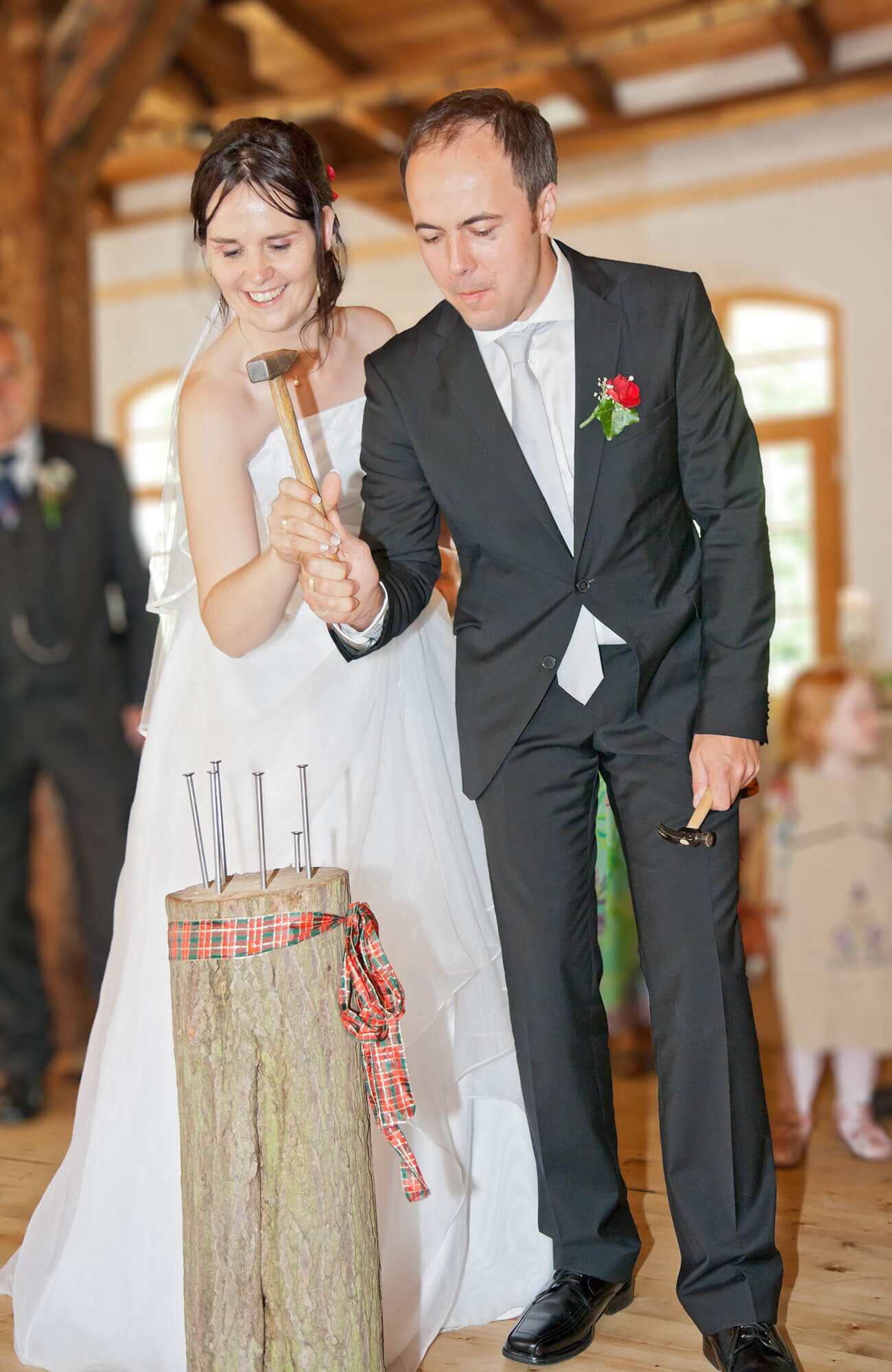 Braut und Bräutigam hämmern Nägel in einen Baumstamm